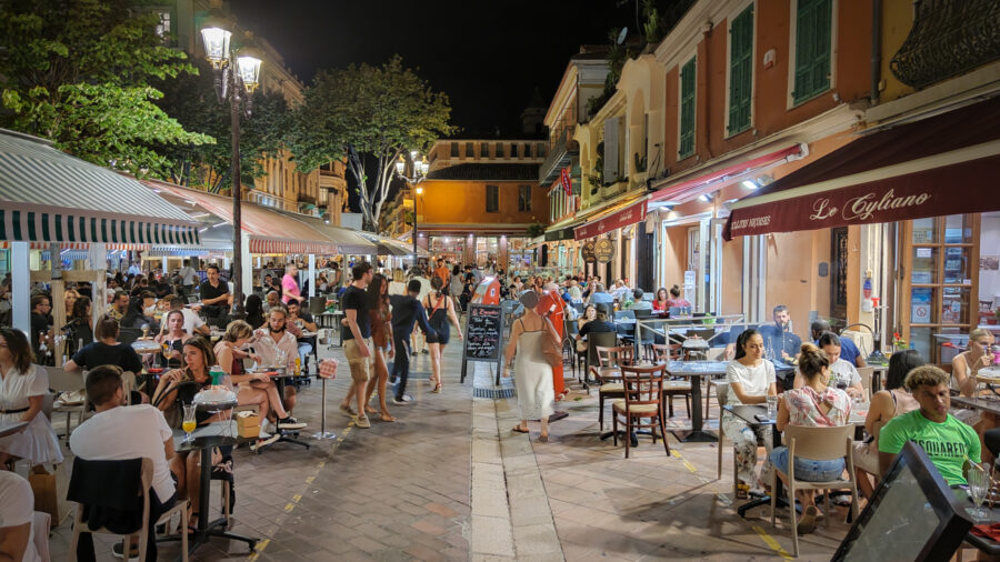 Pedestrian street at night with outdoor cafes, al fresco dining, and warm lamps.