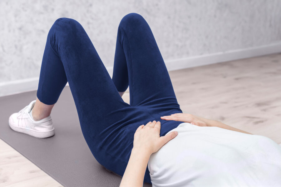Woman reclined on a mat, practicing a pelvic floor exercise, emphasizing her commitment to fitness and well-being