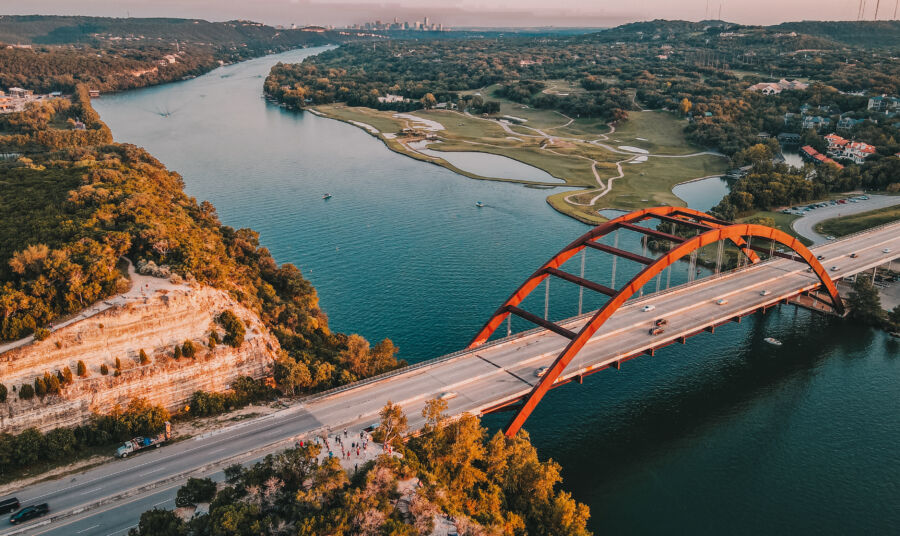 Aerial view of the Austin skyline featuring the Pennybacker Bridge and surrounding cityscape under a clear blue sky.