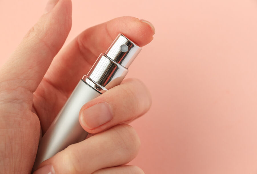 Hand grasping a silver aerosol spray, identified as a perfume atomizer.
