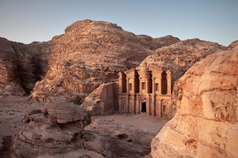 Ancient Petra Monastery carved into sandstone cliffs, surrounded by dramatic natural landscapes at dawn.