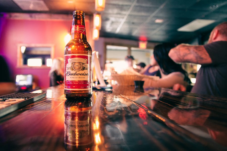 Beer bottle served on counter near anonymous people in pub