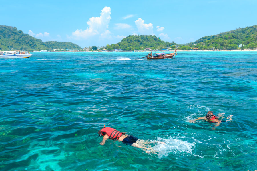 Tourists swim and snorkel in the clear waters of the Andaman Sea at the picturesque Phi Phi Islands in Thailand