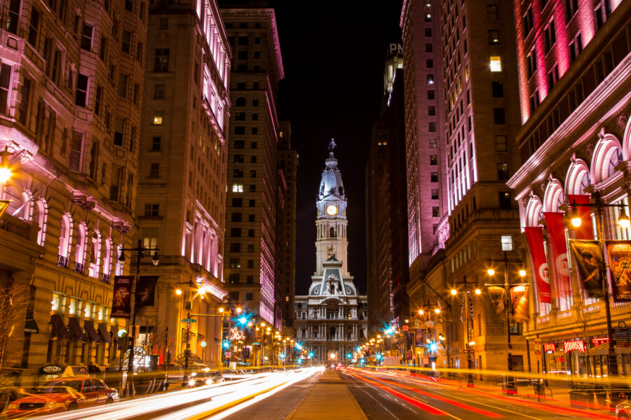 Iconic Philadelphia clock tower at night, vibrant city lights and bustling streets.