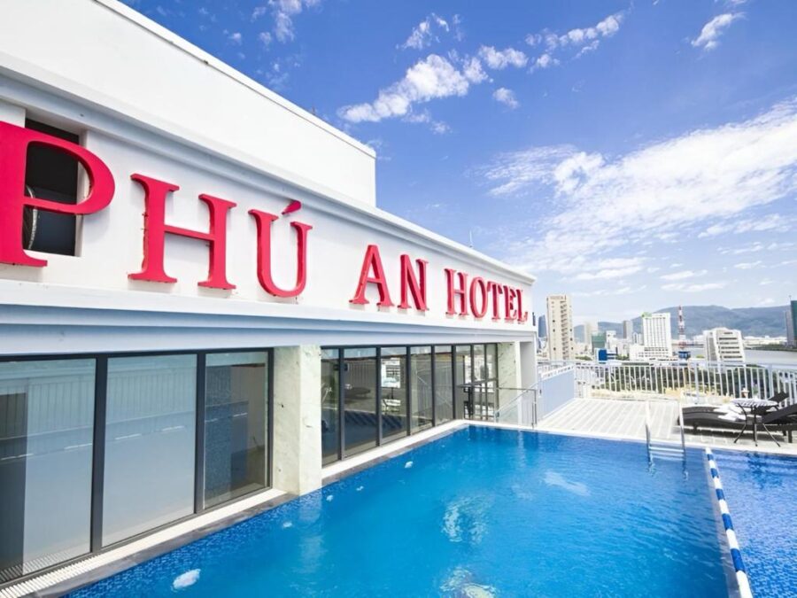 Phu An Hotel rooftop infinity pool with city skyline, modern lounge chairs, umbrellas and mountains.