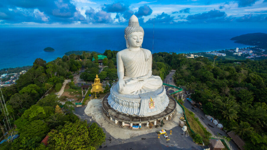 The Phuket Big Buddha stands against a backdrop of a clear blue sky and ocean, emphasizing its majestic presence