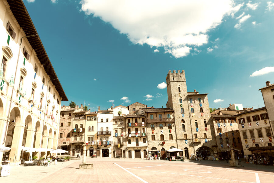Tourists relax and explore Piazza Grande in Arezzo, Italy, surrounded by historic architecture and vibrant atmosphere.