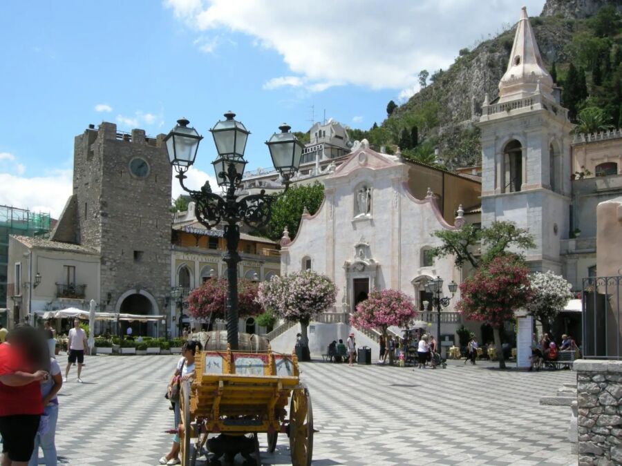 Piazza IX Aprile showcases a church and clock tower in a charming square, surrounded by vibrant local architecture.