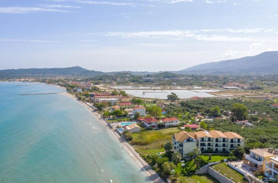 Serene coastal scene with turquoise waters, sandy shores, vibrant architecture, and lush green hills.