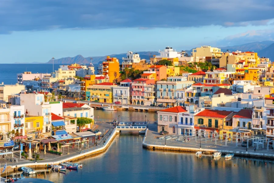 Colorful coastal townscape with harbor, boats, and scenic hills in Agios Nikolaos.