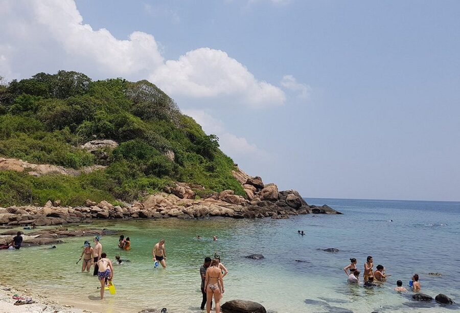 People swim in the ocean near a rocky shore at Pigeon Island National Park, enjoying the clear blue water and scenic views.