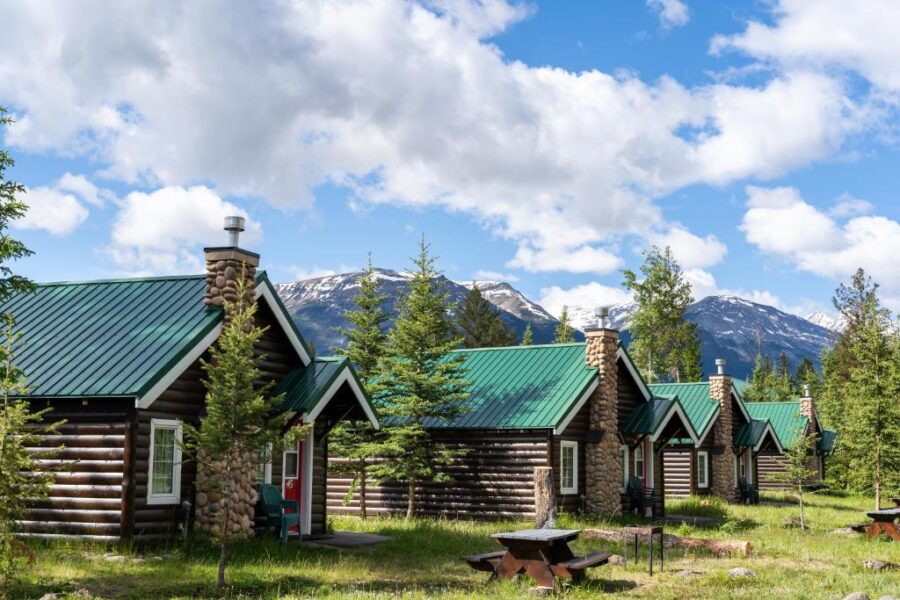 Scenic view of log cabins in the mountains, with lush trees and peaks in the background at Pine Bungalows, Jasper, Canada.
