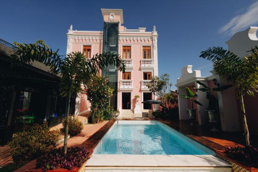 Luxury pink boutique hotel mansion with tropical pool, palm trees, and elegant colonial architecture.
