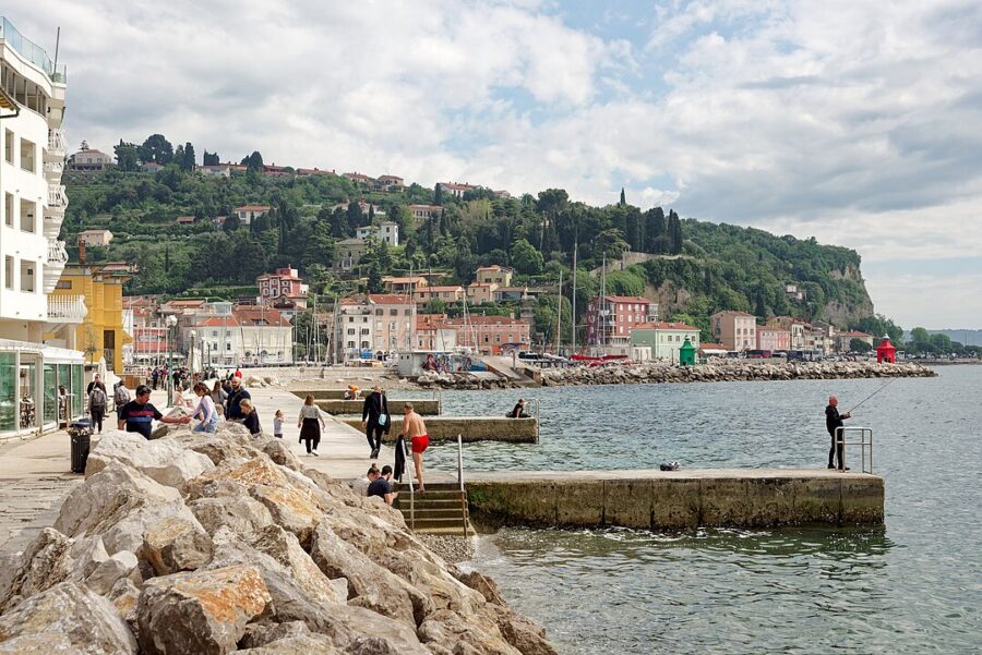People gather on a dock by the water at Piran Harbour, Slovenia, enjoying the scenic view of the harbor.