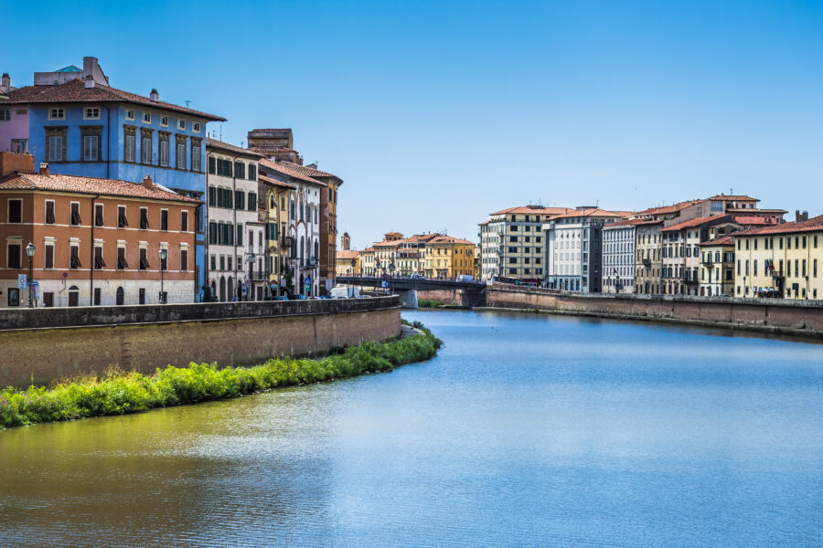 Scenic view of the Arno River in Pisa, Italy, lined with colorful houses reflecting in the water under a clear sky