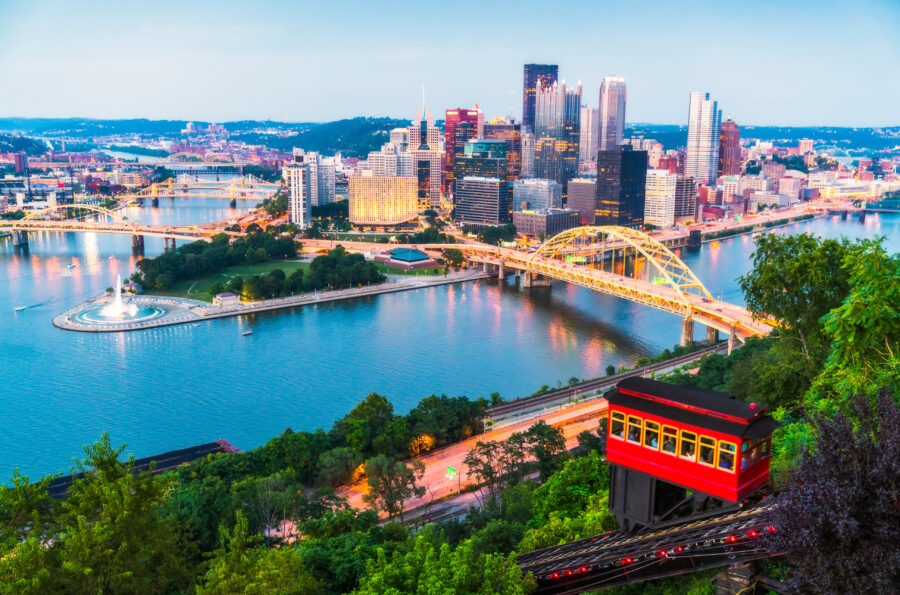 Aerial view of Pittsburgh, Pennsylvania, showcasing the city's skyline, rivers, and bridges under a clear blue sky.