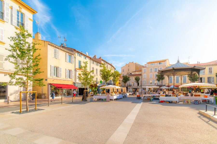 Vibrant outdoor market at Place Amiral Barnaud in Antibes, featuring clothing and flea market stalls along the Mediterranean.