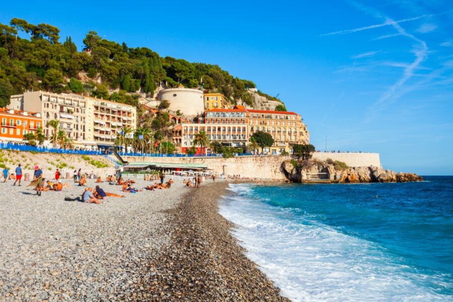 Blue Beach in Nice, France, featuring golden sand, clear blue water, and sun loungers under umbrellas along the shoreline