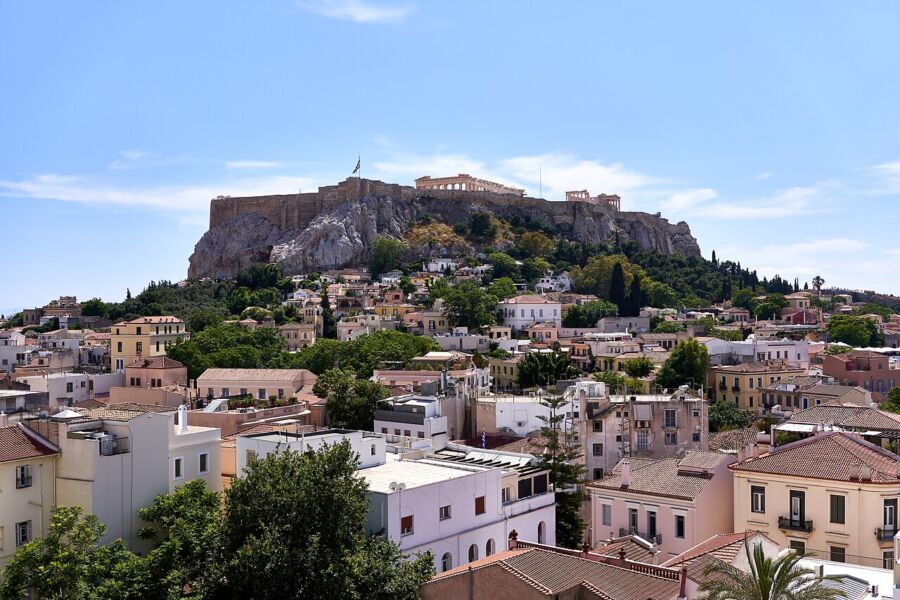 Panoramic view of the Acropolis from a hilltop in Plaka, Greece, showcasing ancient architecture against a clear sky.