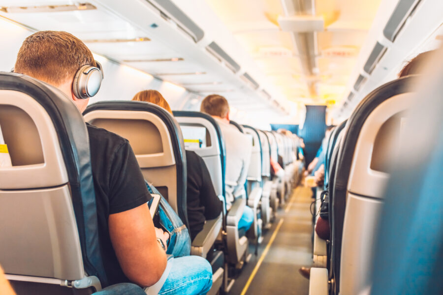 Economy class airplane cabin with passengers seated in armchair-style seats along a central aisle.