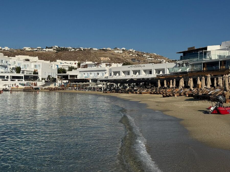 Platis Gialos Beach in Greece, showcasing white buildings and vibrant umbrellas set against the sandy beach.
