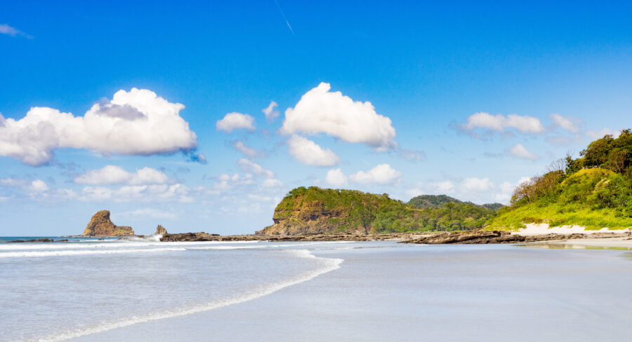 Scenic Playa Maderas beach in San Juan del Sur, featuring golden sand, gentle waves, and lush green hills in the background