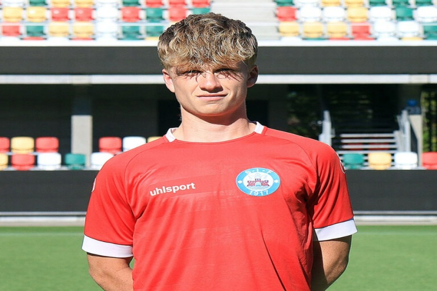 Jeppe Spejlborg in red soccer jersey standing on stadium pitch.