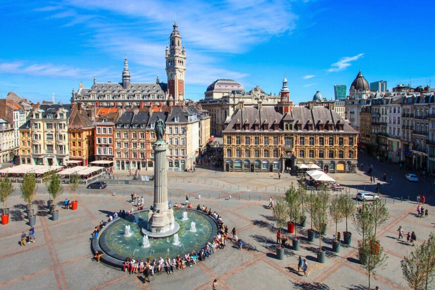 Lille historic square with central fountain and column under bright blue sky.