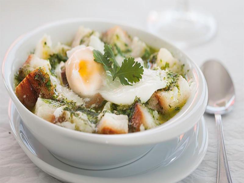 Açorda Alentejana: poached egg on crusty bread with herb sauce in white bowl.
