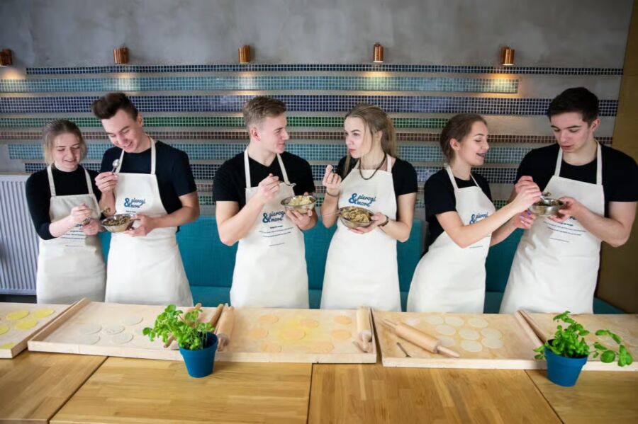 Young individuals in aprons engaged in food preparation at a Polish dumpling cooking class, showcasing teamwork and learning.