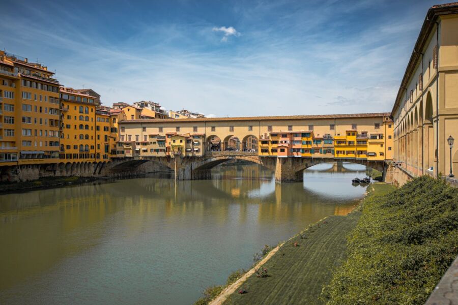 Ponte Vecchio in Florence, Italy, over Arno River with shops and serene reflections.