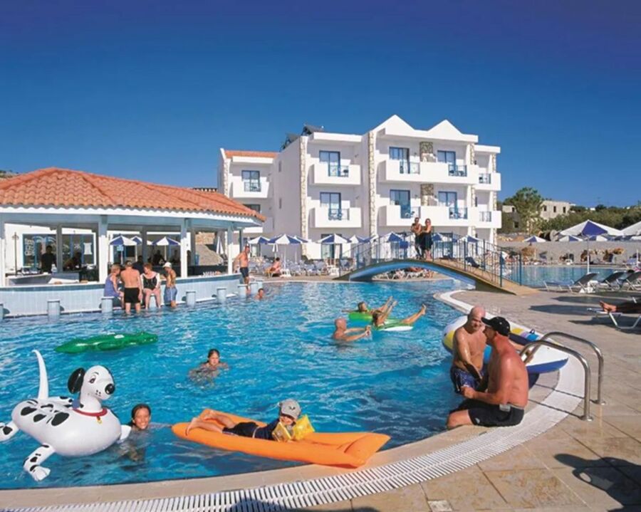 Sunny resort pool scene with guests, inflatable toys, loungers, umbrellas, and Mediterranean architecture.