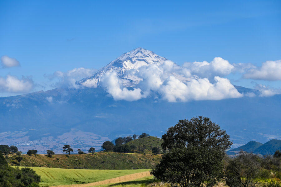 Meadow landscape with Popocatepetl volcano in the background, clear sky, and a visible hiking trail