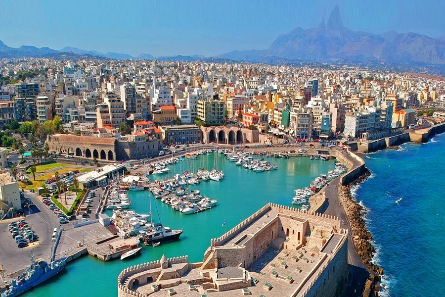 Aerial view of a Mediterranean coastal city with a historic fortress and vibrant harbor.