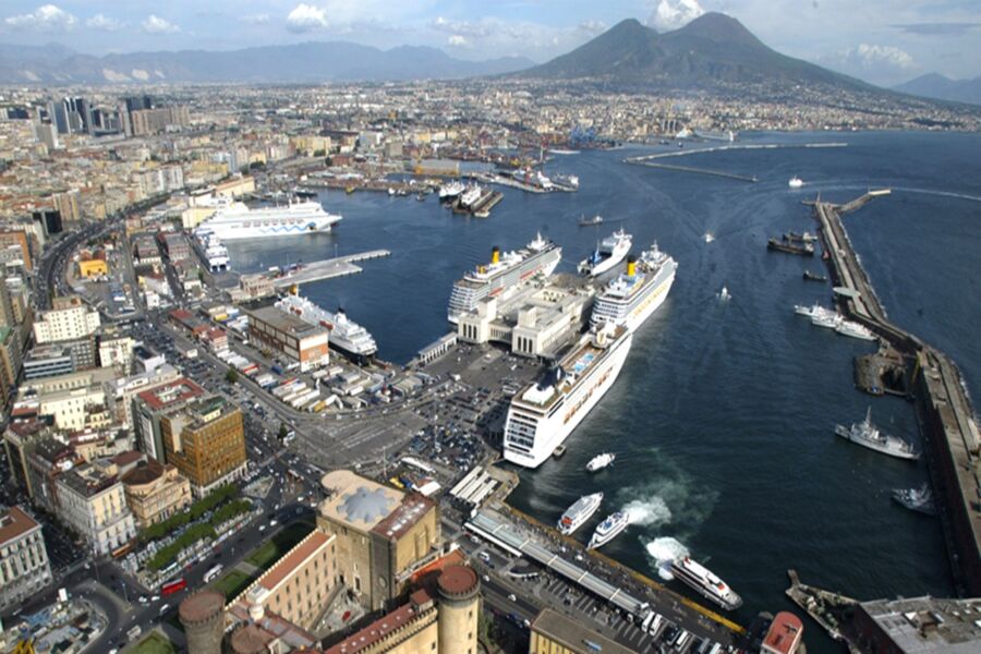 Aerial view of bustling Port of Naples harbor with Mount Vesuvius in the background.