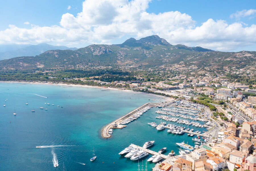 Scenic view of the Port of Calvi in Corsica, featuring boats docked against a backdrop of colorful buildings and mountains.