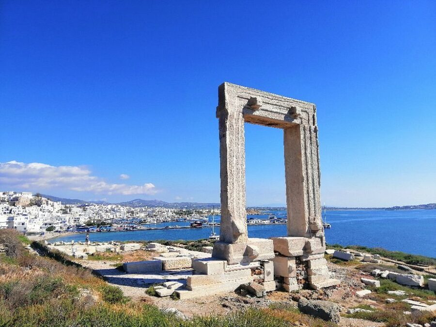 Ancient Portara ruin on Naxos island with Greek coastal town and sea backdrop.