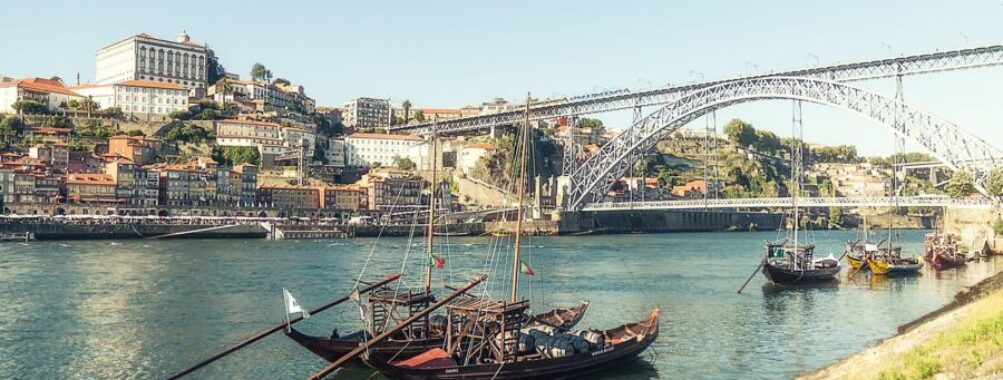 Riverside Porto: historic boats, vibrant buildings, iconic bridge, serene scenery.