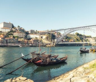 Riverside Porto: historic boats, vibrant buildings, iconic bridge, serene scenery.