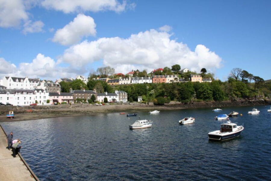 Portree Harbour Front on the Isle of Skye, showcasing a calm body of water with several boats moored along the dock.