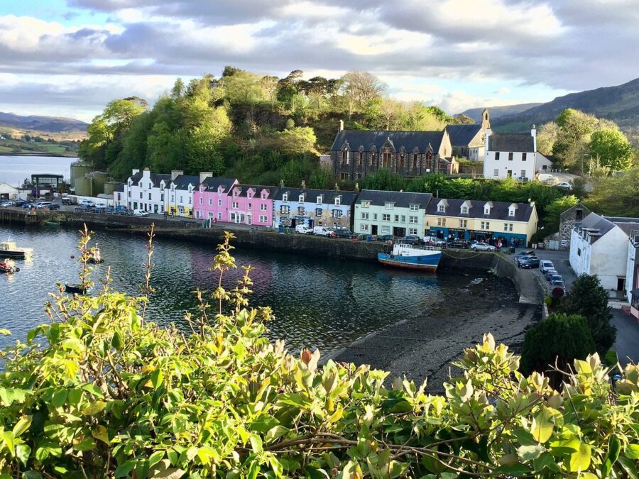 Panoramic view of Portree Harbour, Isle of Skye, from the top of a hill, showcasing colorful buildings and the sea.