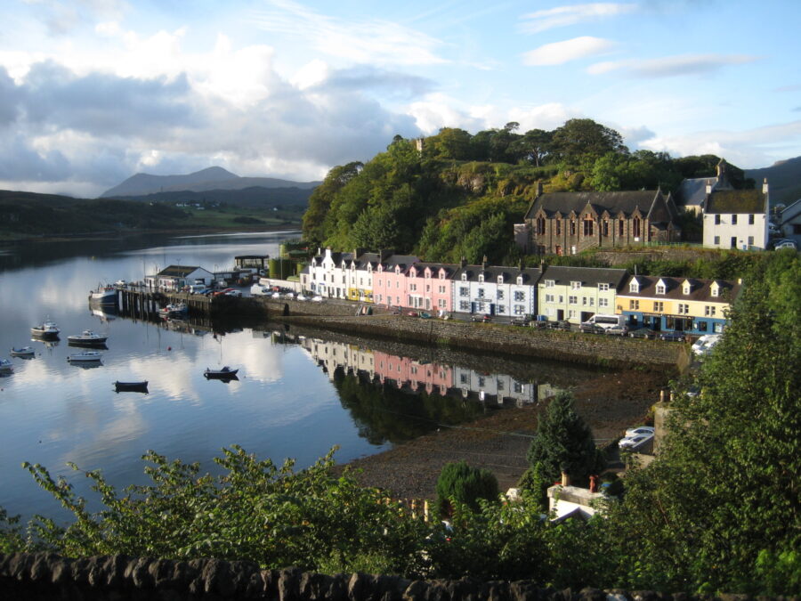 Scenic panorama of a calm body of water in Portree, Isle of Skye, framed by rolling hills and a clear sky.