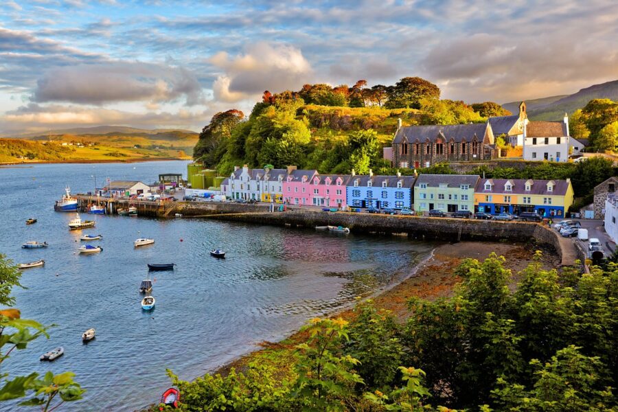 Colorful houses line the shore of a lake at sunset in Portree, Isle of Skye, creating a picturesque scene.