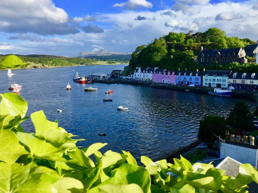Colorful houses line the shore of a lake at sunrise in Portree, Isle of Skye, creating a picturesque panorama.