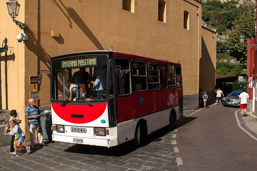 Red and white bus labeled as Positano, standing out in a picturesque coastal setting.