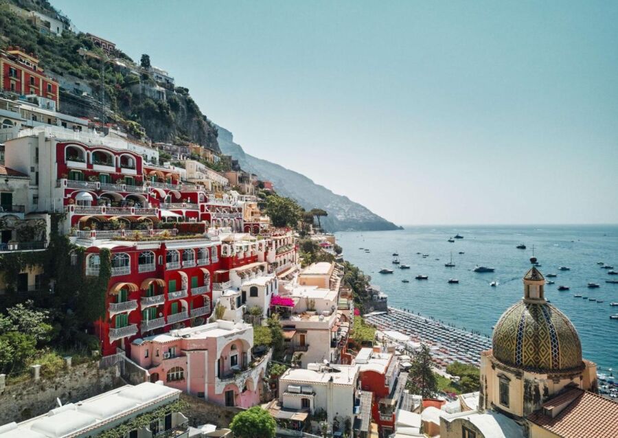 Positanos colorful cliffs, Mediterranean sea boats, and lush greenery create a picturesque coastal view.