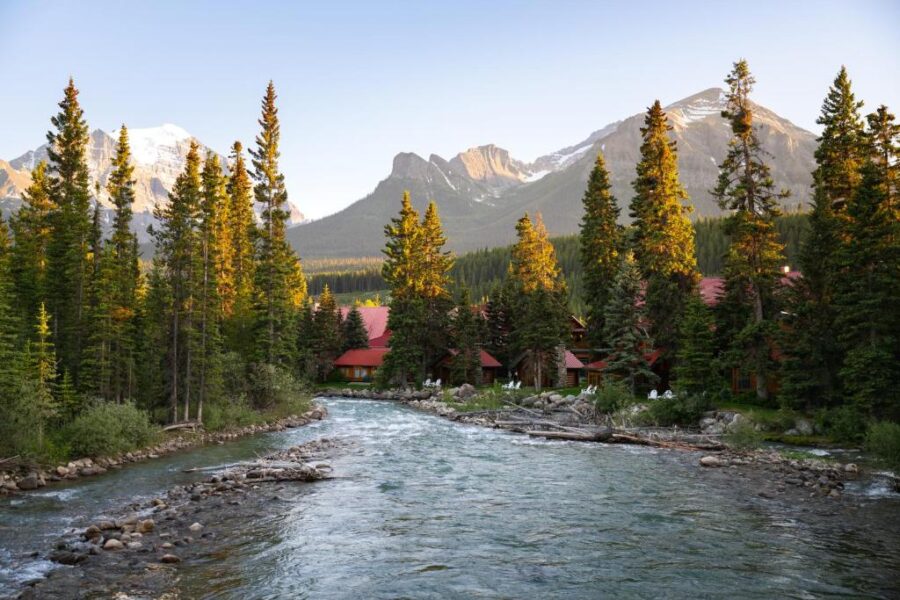 Serene river flows through a lush forest, with majestic mountains rising in the background near Post Hotel & Spa, Canada.
