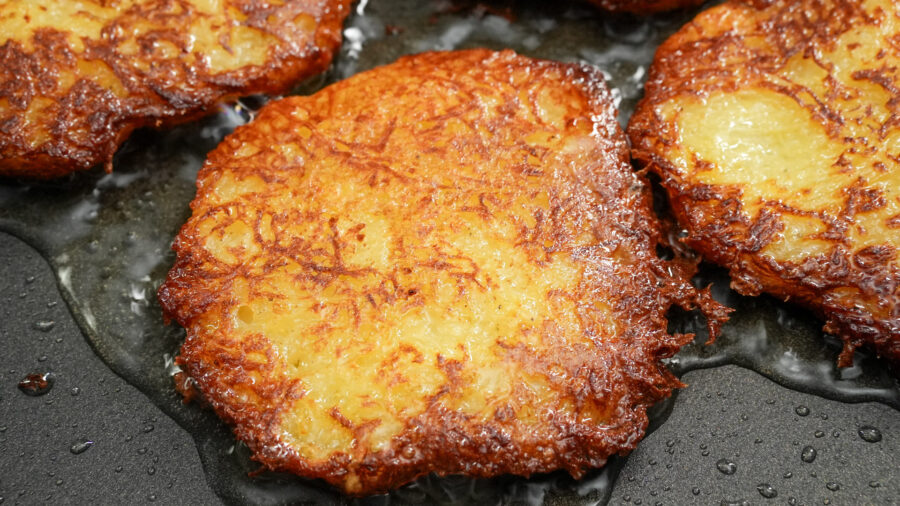 Crispy golden potato pancakes frying in oil, close-up of latkes.