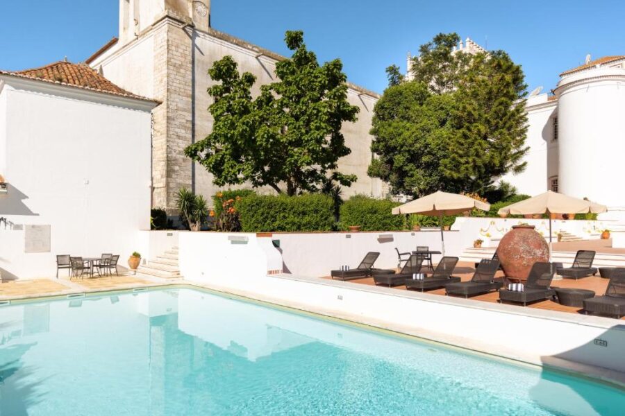 Pousada Castelo de Estremoz's pool area, showcasing a white building and a church tower in the background.