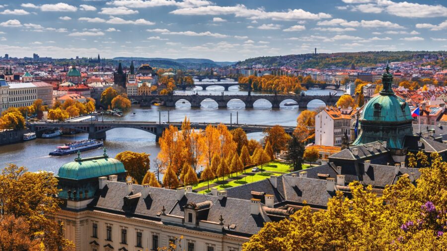 Panoramic view of Prague with Vltava River, Charles Bridge, autumn foliage, iconic architecture.